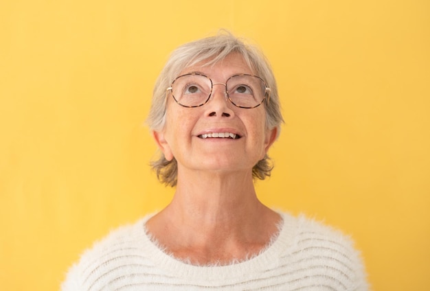 Porträt einer schönen reifen Frau weiß gekleidet mit Brille, die nach oben schaut, auf gelbem Hintergrund