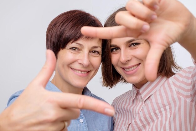 Porträt einer schönen reifen Mutter und ihrer Tochter, die mit den Händen eine Geste machen, als würden sie ein Selfie machen und lächeln