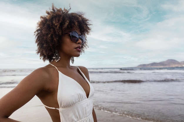 Porträt einer schönen schwarzen Frau mit lockigem Haar, die eine Sonnenbrille am Strand trägt