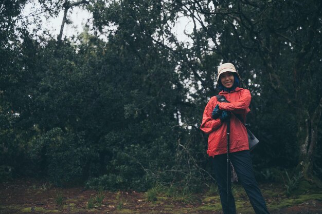 Porträt einer schönen und abenteuerlustigen jungen asiatischen Wanderin in Sportbekleidung mit Helm und Gehstock, die im Wald steht, während sie eine Pause von der Wanderung in den Bergen macht