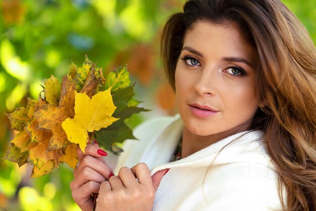 Porträt einer schönen und liebenswerten jungen Frau, die an einem sonnigen Tag gefallene Blätter auf einem verschwommenen Hintergrund des Herbstparks hält