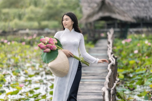 Porträt einer schönen vietnamesischen Frau mit traditionellem Vietnam-Hut, der den rosa Lotus hält