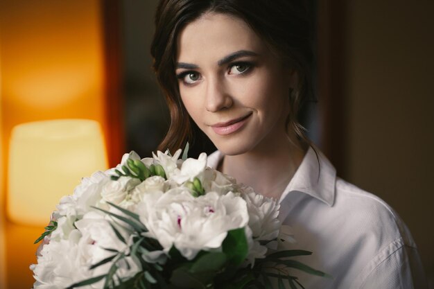 Porträt einer schönen zarten Braut in einem weißen Hemd mit einem Hochzeitsblumenstrauß