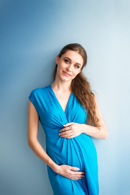 Porträt einer schwangeren Frau in einem blauen Kleid auf einem blauen Hintergrund