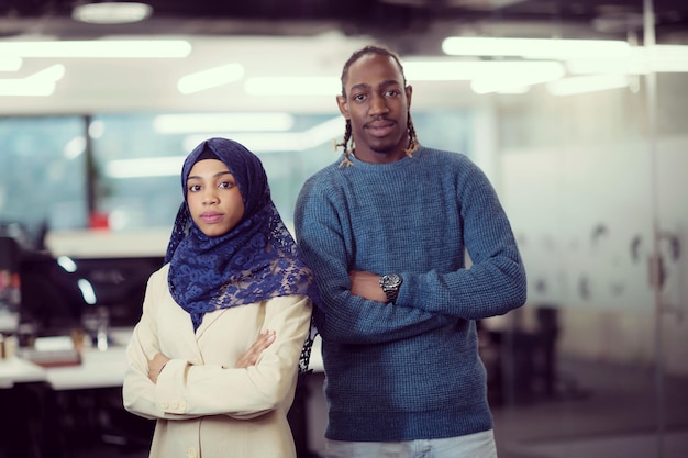Porträt einer schwarzen muslimischen Softwareentwicklerin, die zusammen mit ihrem afroamerikanischen männlichen Kollegen im modernen Startup-Büro steht