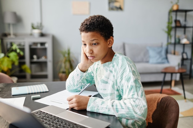 Porträt einer schwarzen Teenagerin, die auf den Laptop-Bildschirm schaut, während sie zu Hause in einer Online-Unterrichtskopie lernt...