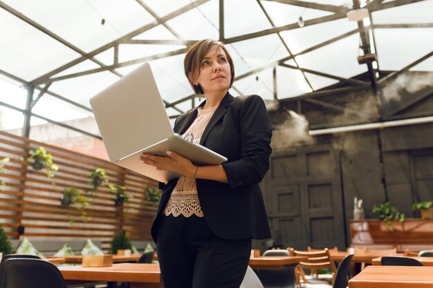 Porträt einer selbstbewussten reifen professionellen Frau, die mit Laptop auf der Sommerterrasse im Café sitzt