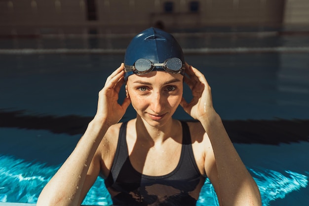 Porträt einer selbstbewussten sportlichen Schwimmerin mit Mütze und Schutzbrille, die in die Kamera blickt