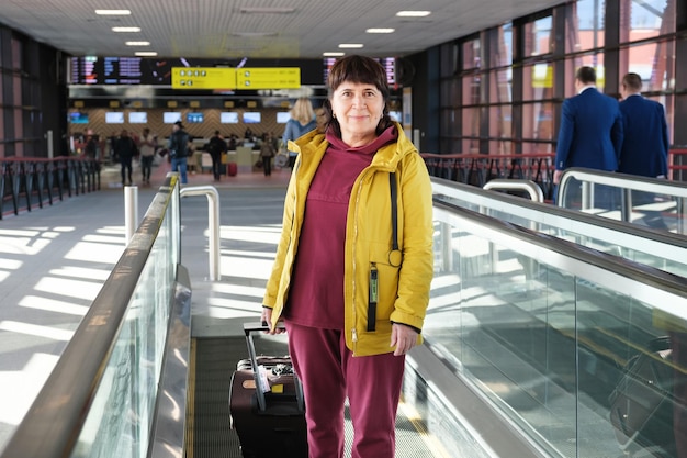 Porträt einer Seniorin mit Koffer am Flughafen