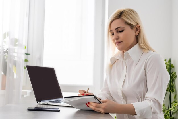 Porträt einer seriösen Geschäftsfrau mit Laptop im Büro vor einer weißen Wand