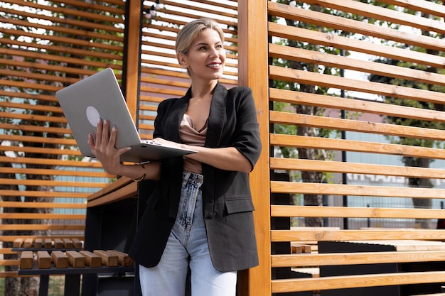 Porträt einer starken Geschäftsfrau, die mit Laptop in der Nähe einer Holzwand im Freien Geld verdient