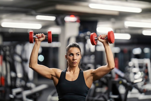 Porträt einer starken muskulösen Bodybuilderin, die Hanteln in einem Fitnessstudio hebt