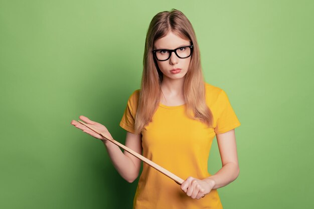 Porträt einer strengen, ernsthaften Lehrerin, die einen Zeiger trägt, eine Brille trägt ein gelbes T-Shirt, das die Kamera stirnrunzelnd aussieht