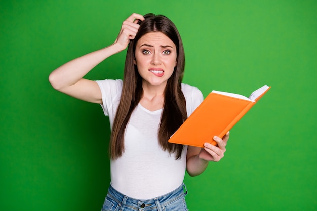 Porträt einer süßen verwirrten jungen Frau, die ein Buch hält, das nicht versteht, ein lässiges T-Shirt zu tragen, das auf grünem Hintergrund isoliert ist