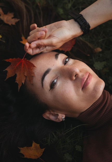 Porträt einer traurigen, schönen jungen Frau, die auf dem Boden eines Herbstwaldes mit bunten Ahornblättern liegt Konzept blauer Montag