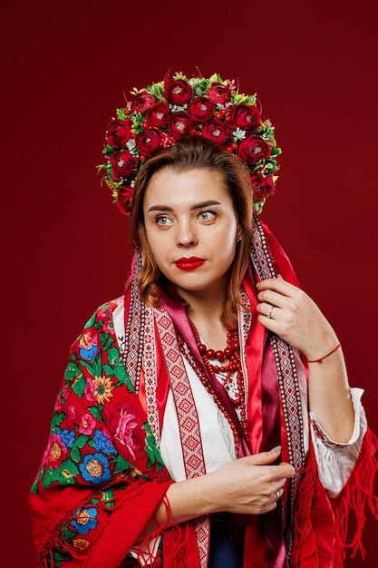 Porträt einer ukrainischen Frau in traditioneller ethnischer Kleidung und rotem Blumenkranz auf viva magenta Studiohintergrund Ukrainische nationale bestickte Kleidung rufen Vyshyvanka an. Beten Sie für die Ukraine