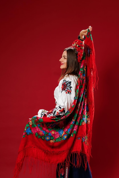 Porträt einer ukrainischen Frau in traditioneller ethnischer Kleidung und rotem Blumenkranz auf viva magentafarbenem Studiohintergrund wirbelt ein Taschentuch