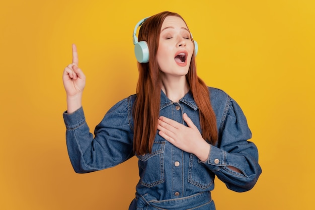 Porträt einer unabhängigen Dame mit Kopfhörern, die Musik hört, die Augen schließen, ein Lied auf gelbem Hintergrund singen