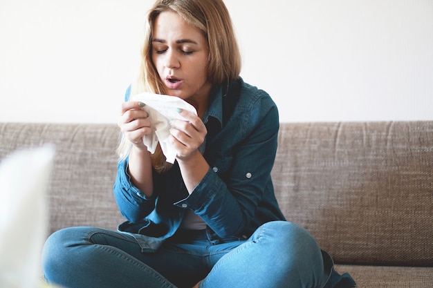 Porträt einer ungesunden süßen blonden Frau mit Serviette, die Nase weht, schaut auf die Quelle der Allergie. Rhinitis, Erkältung, Allergiekonzept