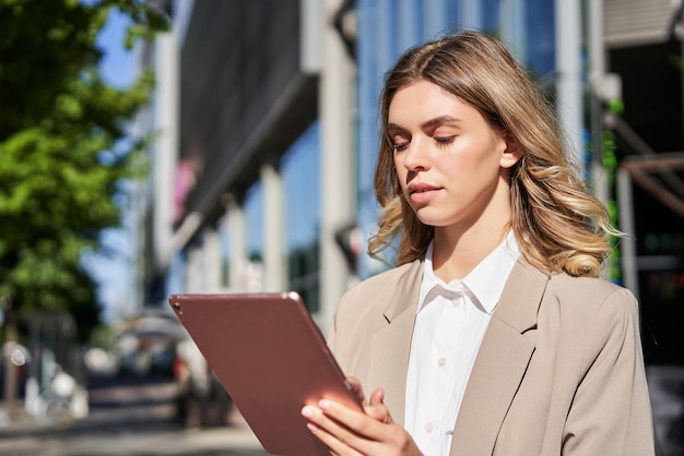 Porträt einer Unternehmensfrau liest Nachrichten auf ihrem digitalen Tablet, während sie auf dem Weg zum Bürostand ist