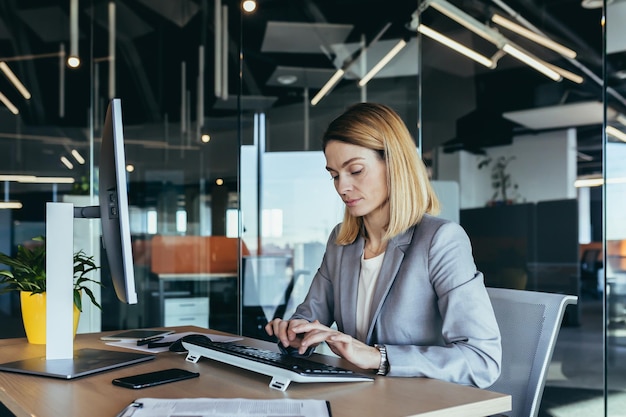 Porträt einer vernünftigen und fairen erfolgreichen Geschäftsfrau, die selbstbewusst und konzentriert in einem modernen Büro am Computer arbeitet