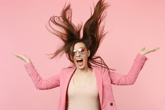 Porträt einer verrückten schreienden jungen Frau mit Herzbrille, die mit flatterndem Haar springt, isoliert auf pastellrosa Wandhintergrund im Studio. Menschen aufrichtige Emotionen Lifestyle-Konzept. Mock-up-Kopienbereich.