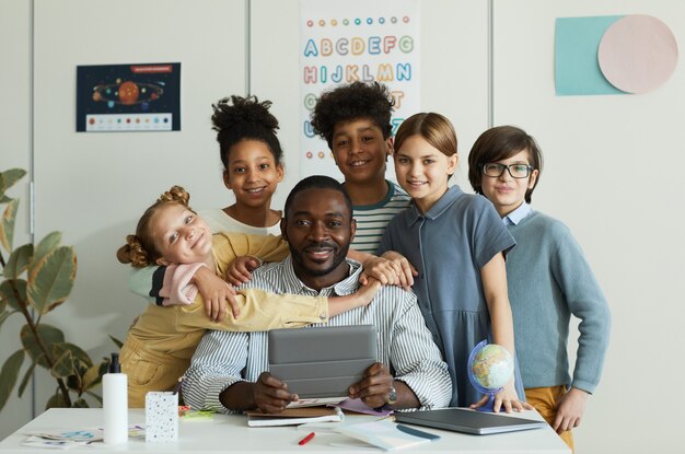 Porträt einer verschiedenen Gruppe von Kindern mit männlichem Lehrer, der die Kamera im Schulklassenzimmer betrachtet