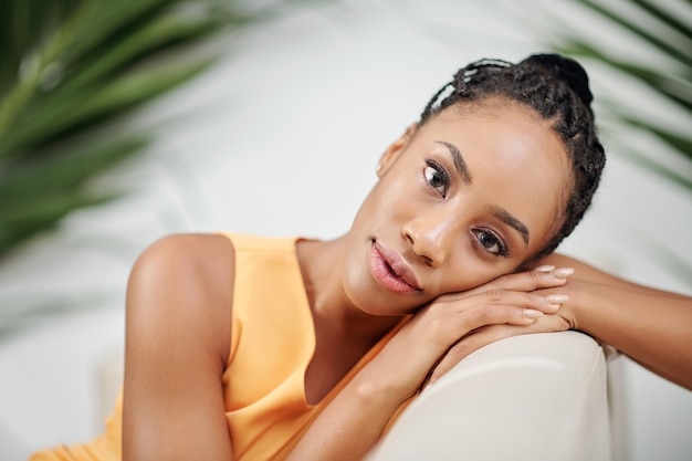 Porträt einer verträumten jungen schwarzen Frau, die sich auf ihrem Stuhl lehnt