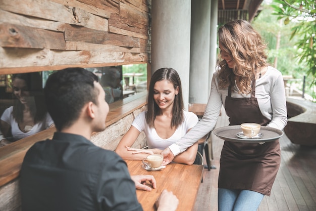 Porträt einer weiblichen Kellnerin, die einem Paar Kunden Kaffee serviert