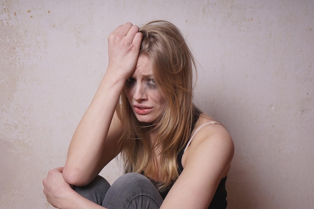 Porträt einer weinenden jungen Frau, die an der Wand sitzt