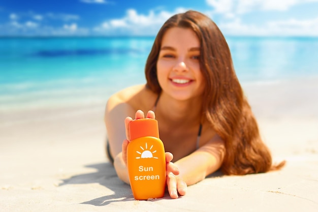 Porträt einer wunderschönen Frau, die lächelt, während sie sich am Strand entspannt und eine Sonnenschutzflasche hält