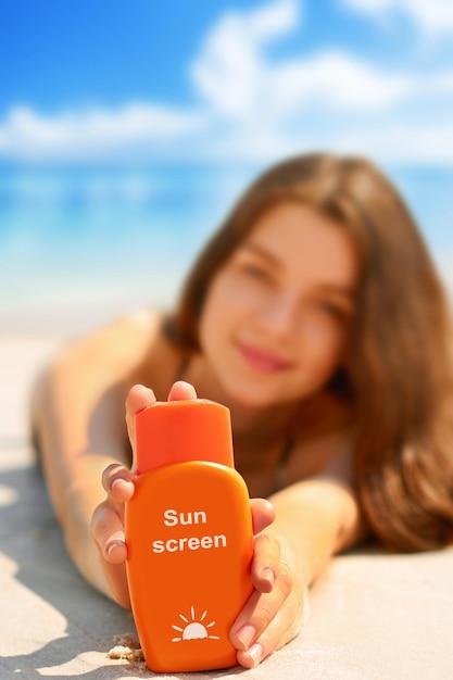 Porträt einer wunderschönen jungen Frau, die lächelt, während sie sich am Strand entspannt und eine Sonnenschutzflasche hält