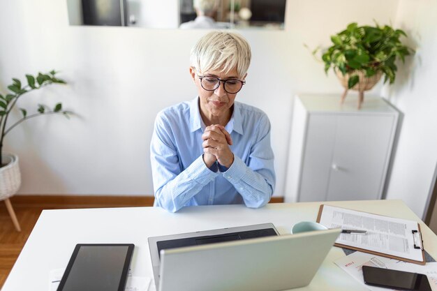 Porträt einer zufälligen Frau, die ihren Laptop benutzt, während sie im Home Office sitzt und arbeitet. Eine attraktive Geschäftsfrau mittleren Alters, die vor einem Laptop sitzt und ihr kleines Unternehmen von zu Hause aus verwaltet.