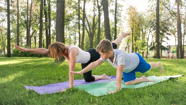 Porträt eines 12-jährigen jungen, der mit seiner mutter im park yoga-übungen macht. familie meditiert und streckt sich im wald