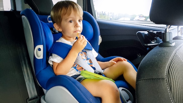 Porträt eines 3 Jahre alten Kleinkindjungen, der im Kindersitz im Auto sitzt und Kekse isst. Kinder reisen im Auto