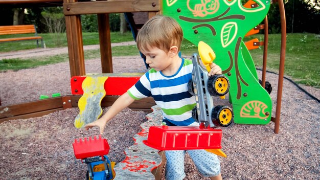 Porträt eines 3 Jahre alten Kleinkindjungen, der seine Spielsachen aus dem Sandkasten in Palyground nimmt