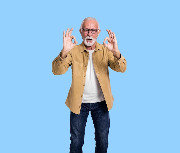 Porträt eines älteren männlichen Unternehmers, der OK-Schilder zeigt und auf blauem Hintergrund fröhlich schreit