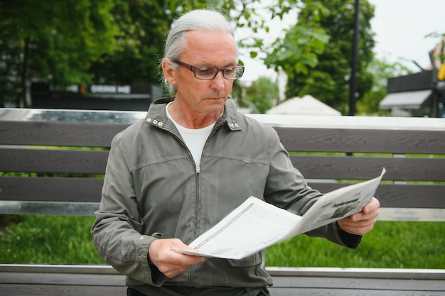 Porträt eines älteren Mannes, der während des Sommertages auf der Bank liest