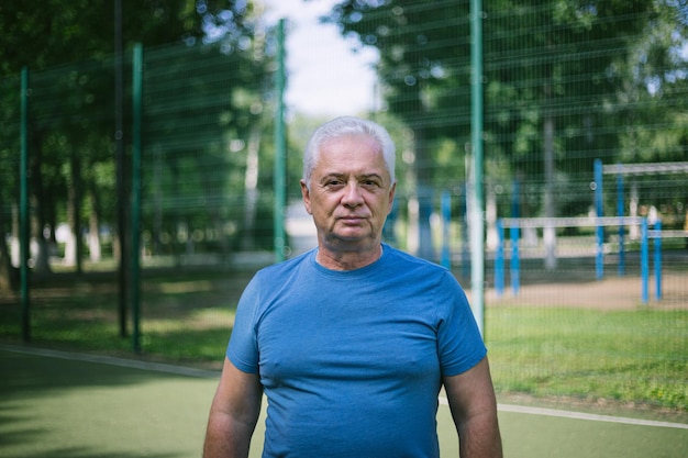 Porträt eines älteren Mannes über 50 mit grauen Haaren in einem Sporttrikot auf einem Sportplatz