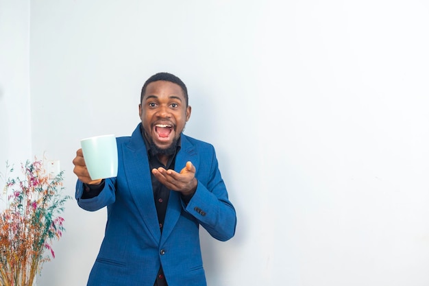 Porträt eines afrikanischen jungen Geschäftsmannes mit fröhlicher Stimmung, der eine Kaffeetasse hält und einen Business-Anzug trägt