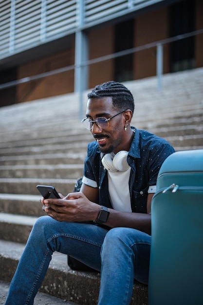 Porträt eines afrikanischen Mannes, der soziale Medien auf seinem Smartphone außerhalb eines Bahnhofs nutzt