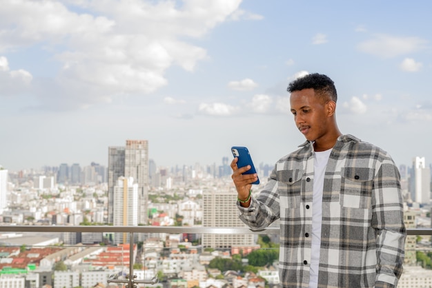 Porträt eines afrikanischen schwarzen Mannes draußen in der Stadt auf dem Dach im Sommer mit horizontaler Aufnahme des Mobiltelefons
