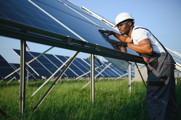 Porträt eines afroamerikanischen Elektroingenieurs in Sicherheitshelm und Uniform, der Solarmodule installiert