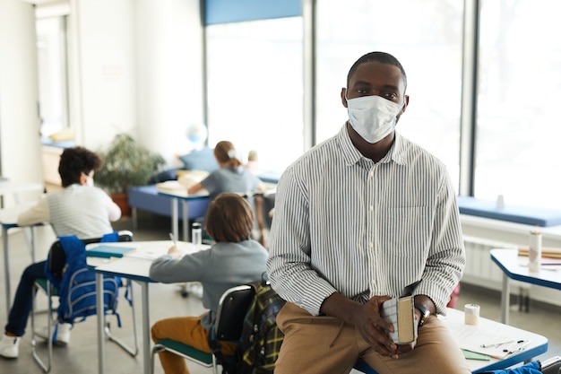 Porträt eines afroamerikanischen Lehrers, der im Schulklassenzimmer eine Maske trägt und in die Kamera schaut, Platz kopieren