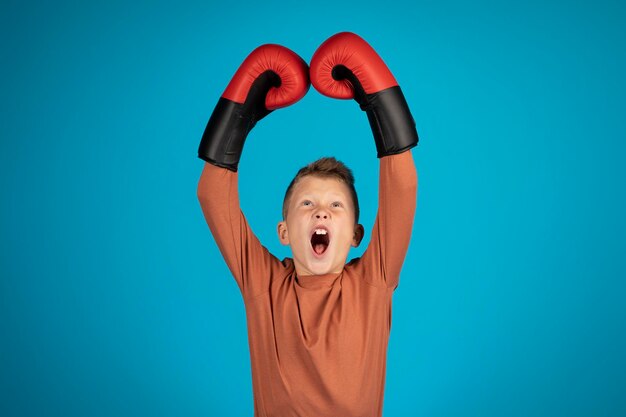 Porträt eines aggressiven jugendlichen Jungen, der Boxhandschuhe trägt, die Arme anhebt und schreit