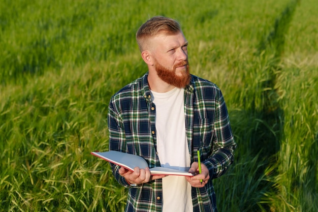 Porträt eines Agronomen mit Notizbuch in einem Weizenfeld Ein Bauer mit Bart und Hemd bereitet das Feld für die zukünftige Ernte vor