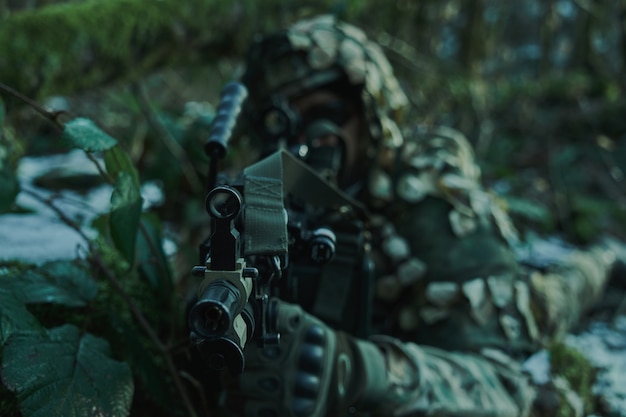 Porträt eines Airsoft-Spielers in professioneller Ausrüstung im Helm, der auf ein Opfer mit einer Waffe im Wald abzielt. Soldat mit Waffen im Krieg