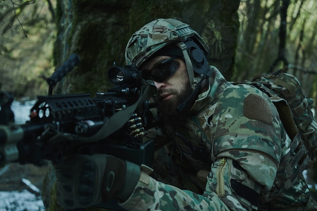 Porträt eines Airsoft-Spielers in professioneller Ausrüstung im Helm, der auf ein Opfer mit einer Waffe im Wald abzielt. Soldat mit Waffen im Krieg