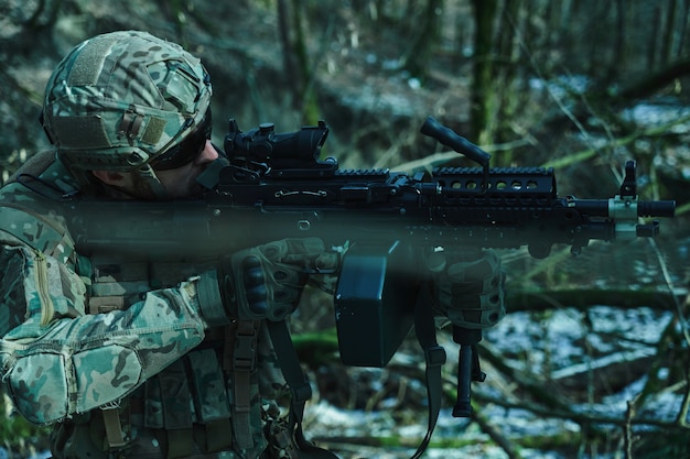 Porträt eines Airsoft-Spielers in professioneller Ausrüstung im Helm, der auf ein Opfer mit einer Waffe im Wald abzielt. Soldat mit Waffen im Krieg