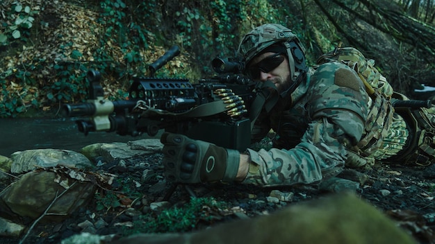 Porträt eines Airsoft-Spielers in professioneller Ausrüstung im Helm, der auf ein Opfer mit einer Waffe im Wald abzielt. Soldat mit Waffen im Krieg